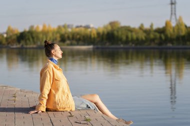 Genç bir kadın setin kenarında nehrin kenarında oturuyor. Kavram: özgürlük, hayatın tadını çıkarmak, kendinle baş başa kalmak. Yüksek kalite fotoğraf