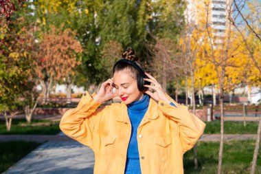 Kulaklıklı genç bir kadın müzik dinler ve sonbahar parkında yürür. Yüksek kalite fotoğraf