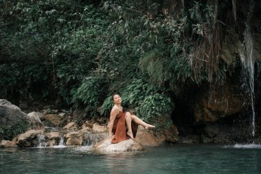 Hindistan, Gizli Şelale. Kahverengi elbiseli Asyalı bir kız, tropiklerin arka planında. Yüksek kalite fotoğraf.