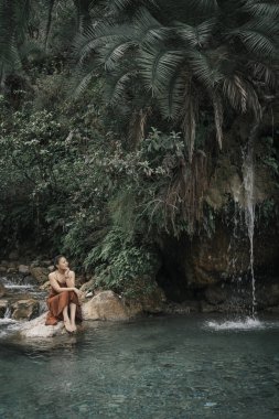 Hindistan, Gizli Şelale. Kahverengi elbiseli Asyalı bir kız, tropiklerin arka planında. Yüksek kalite fotoğraf.