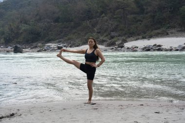 Hindistan, Rishikesh, 27 Mart 2024. Asyalı güzel genç kadın Ganj yakınlarında yoga yapıyor. Yüksek kalite fotoğraf