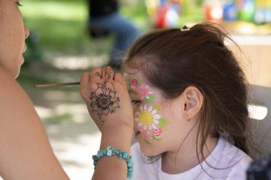 Ressam, kızın yüzüne bir yüz resmi çiziyor. Yüksek kalite fotoğraf. Yüksek kalite fotoğraf