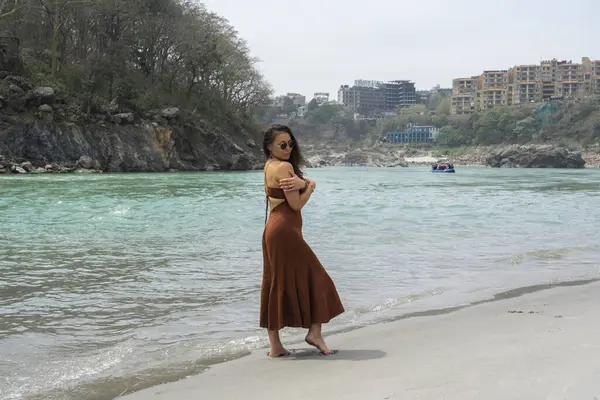 Asyalı bir kadın Ganga Nehri yakınlarındaki sahil boyunca yemek yer ve yürür. Hindistan, Rishikesh. Yüksek kalite fotoğraf