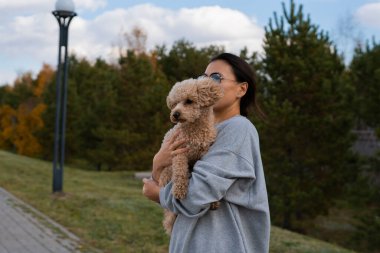 Genç bir Asyalı kadın evcil hayvanını, oyuncak bir kanişi kollarında tutuyor. Sonbahar yürüyüşü. Yüksek kalite fotoğraf