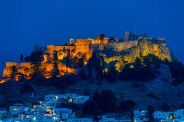 Yunanistan 'ın Rodos adasındaki geleneksel beyaz evlere bakan Lindos Akropolünün günbatımı manzarası.