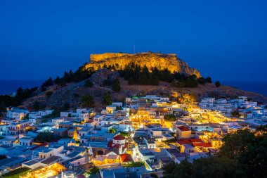 Yunanistan 'ın Rodos adasındaki geleneksel beyaz evlere bakan Lindos Akropolünün günbatımı manzarası.