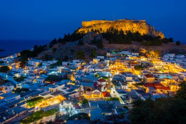 Yunanistan 'ın Rodos adasındaki geleneksel beyaz evlere bakan Lindos Akropolünün günbatımı manzarası.