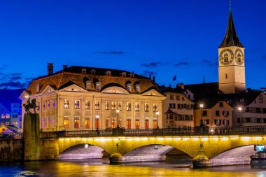 Zuerich, İsviçre 'deki Aziz Peter Kilisesi ve Muensterbruecke' nin gün batımı manzarası.