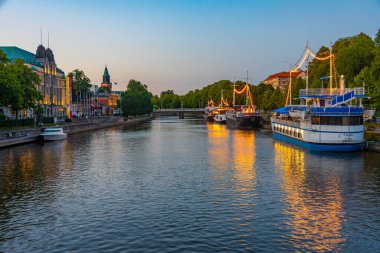 Turku, Finlandiya, 19 Temmuz 2022: Turku, Finlandiya 'da Aura nehri kıyısında demirleyen teknelerin gün batımı manzarası.