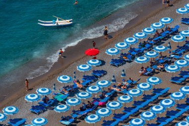 Positano, İtalya, 21 Mayıs 2022: İtalya 'daki Positano plajında mavi ve beyaz şemsiyeler.