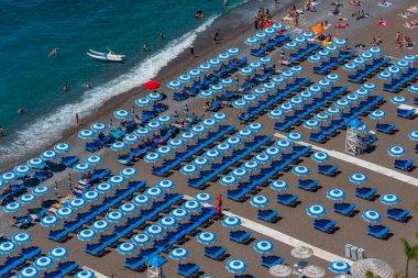 Positano, İtalya, 21 Mayıs 2022: İtalya 'daki Positano plajında mavi ve beyaz şemsiyeler.