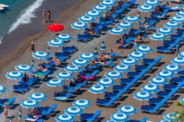 Positano, İtalya, 21 Mayıs 2022: İtalya 'daki Positano plajında mavi ve beyaz şemsiyeler.