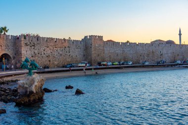 Rodos, Yunanistan, 27 Ağustos 2022: Yunanistan 'da Rodos' ta antik bir kalenin önündeki bir yunus heykelinin gün batımı manzarası.