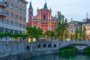 Slovenya 'nın Ljubljana kentindeki Ljubljanica nehrinin nehir kenarındaki Annunciation Kilisesi' nin gün batımı manzarası