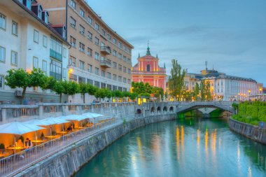 Slovenya 'nın Ljubljana kentindeki Ljubljanica nehrinin nehir kenarındaki Annunciation Kilisesi' nin gün batımı manzarası
