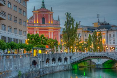 Slovenya 'nın Ljubljana kentindeki Ljubljanica nehrinin nehir kenarındaki Annunciation Kilisesi' nin gün batımı manzarası
