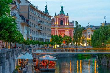 Slovenya 'nın Ljubljana kentindeki Ljubljanica nehrinin nehir kenarındaki Annunciation Kilisesi' nin gün batımı manzarası
