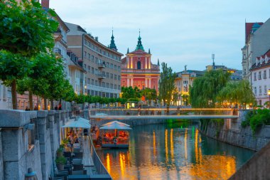Slovenya 'nın Ljubljana kentindeki Ljubljanica nehrinin nehir kenarındaki Annunciation Kilisesi' nin gün batımı manzarası