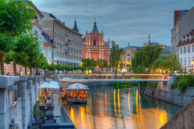 Slovenya 'nın Ljubljana kentindeki Ljubljanica nehrinin nehir kenarındaki Annunciation Kilisesi' nin gün batımı manzarası