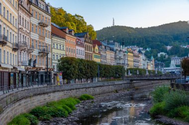 Karlovy Vary, 7 Eylül 2024: Çek Cumhuriyeti 'nin Karlovy Vary kentindeki Tepla nehrine yansıyan renkli evlerin gün batımı görüntüsü.