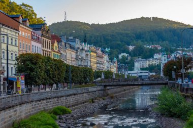 Karlovy Vary, 7 Eylül 2024: Çek Cumhuriyeti 'nin Karlovy Vary kentindeki Tepla nehrine yansıyan renkli evlerin gün batımı görüntüsü.