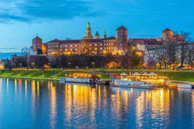 Polonya 'nın Krakow / Krakow kentindeki aydınlanmış Wawel şatosu gece boyunca Vistula / Wisla nehrine yansıdı.