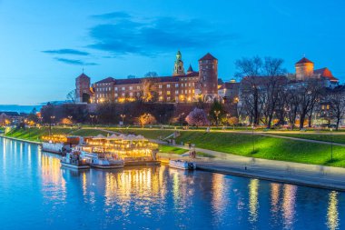 Polonya 'nın Krakow / Krakow kentindeki aydınlanmış Wawel şatosu gece boyunca Vistula / Wisla nehrine yansıdı.