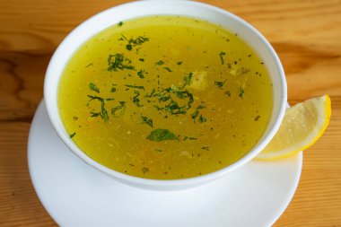 Çorba, ahşap bir masada beyaz bir tabakta servis edilir.