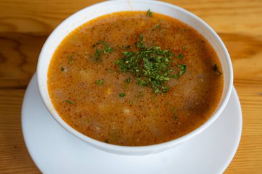 Çorba, ahşap bir masada beyaz bir tabakta servis edilir.