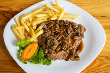 Soslu mantar ve patates kızartması tabakta servis edilir.