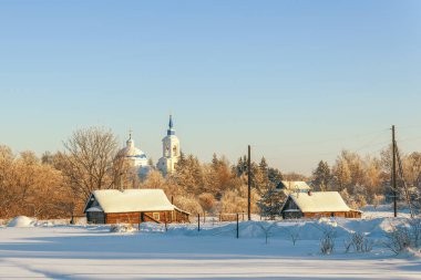 Soğuk bir kış gününde odunluk kulübeleri ve astım kilisesi olan kırsal alan. Pogost Samuru. Novgorod Oblastı. Rusya