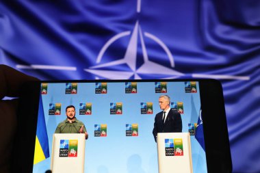 Viewing on the phone the live broadcast from the joint press conference of the President of Ukraine Volodymyr Zelenskyy and NATO Secretary General Jens Stoltenberg during the 2023 NATO Summit in Vilnius, Lithuania, on July 12, 2023 clipart