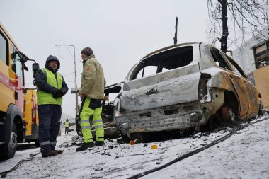 KYIV, UKRAINE - 20240103: Kyivgaz çalışanları, 3 Ocak 2024 'te Ukrayna' nın başkenti Kyiv 'de yapılan bir Rus füze saldırısı sonrasında yanan bir arabanın yanında duruyor. 2 Ocak sabahı, Rus kuvvetleri Kyiv 'e büyük bir füze saldırısı düzenledi..