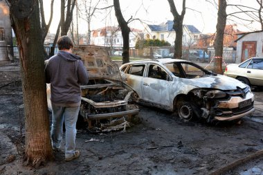 Yerel halk, 21 Mart 2024 'te Kyiv' de meydana gelen saldırıdan sonra roket enkazının düştüğü yerin yakınlarında yanan arabaları inceliyor..