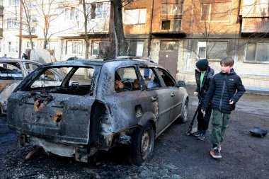 Yerel halk, 21 Mart 2024 'te Kyiv' de meydana gelen saldırıdan sonra roket enkazının düştüğü yerin yakınlarında yanan arabaları inceliyor..