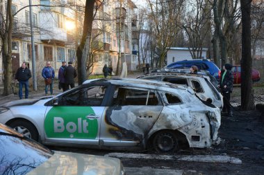 Yerel halk, 21 Mart 2024 'te Kyiv' de meydana gelen saldırıdan sonra roket enkazının düştüğü yerin yakınlarında yanan arabaları inceliyor..