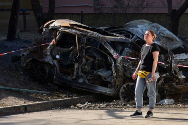 KYIV, UKRAINE - 20240709: Bir kadın, Kyiv 'deki Rus füze saldırısı sonucu yıkılan Holosiivskyi bölgesindeki beş katlı bir konut binasının yakınındaki yanmış bir arabanın arka planında duruyor