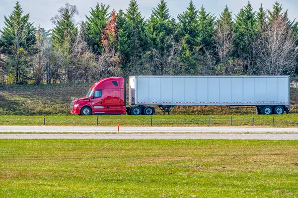 Horizontal shot of a red tractor trailer traveling on a lonely late summer highway.