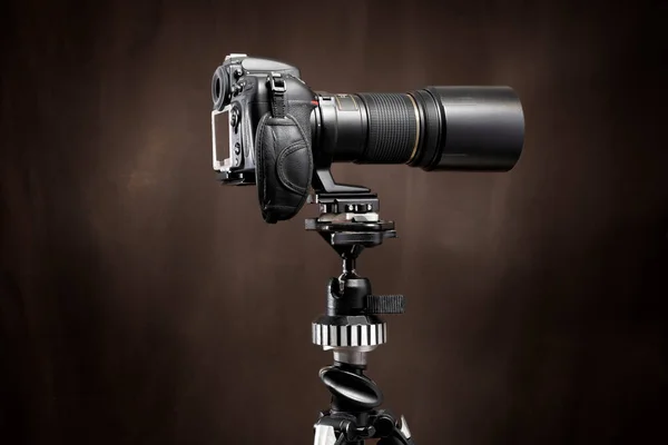 Horizontal side shot of a Digital Single Lens Reflex camera with long lens on a tripod with a brown background with copy space