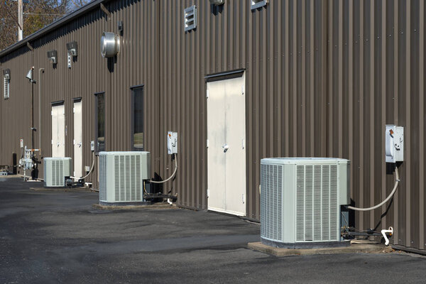 A row of generic air conditioner compressors behind a strip office building