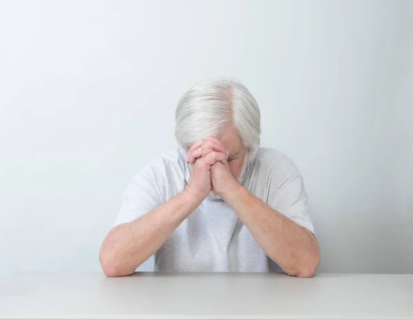 Horizontal shot of a white haired man sitting alone in sadness, prayer or worry.  White background.  Lots of copy space.