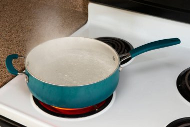 Horizontal shot looking down on a blue pot on a white stove top on a red hot burner holding boiling water. 