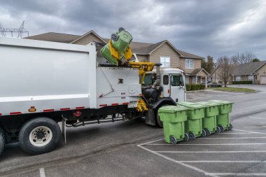 Horizontal shot of a garbage truck picking up and dumping residential trash containers.