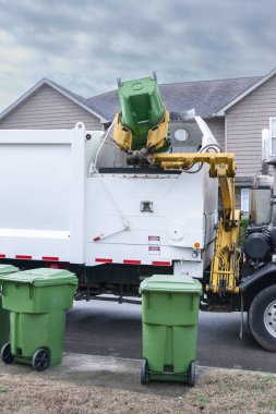 Vertical shot of a mechanized garbage truck dumping trash from residential barrel.