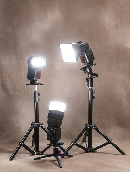 Vertical shot of three radio-controlled electronic strobes on tripods firing in unison on a canvas background.
