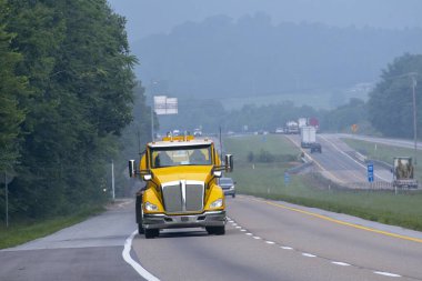 Tennessee 'de yaz mevsimi sisinde tepeye tırmanan sarı bir benzin tankerinin yatay çekimi..