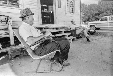 Makedonya, Arkansas, ABD 23 Haziran 2024: 1970 'lerin eski bir taşra mağazasının önünde oturup konuşan iki adamın yatay çekimi.