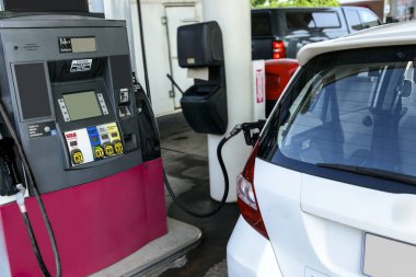 Horizontal close-up shot of a small white car getting gasoline from a gas nozzle. clipart