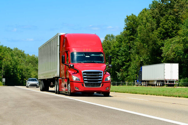 Horizontal shot of a red eighteen wheeler semi on the interstate with copy space. Heat waves rising from the hot asphalt creates a blurring effect on background trucks and foreground pavement.