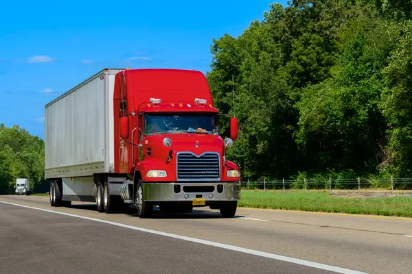 stock image Knoxville, TN, United States  August 20, 2024: horizontal shot of a red eighteen wheeler semi on an interstate highway in the summer heat. Heat waves rising from the hot asphalt creates a blurring effect on background trucks and foreground pavement.